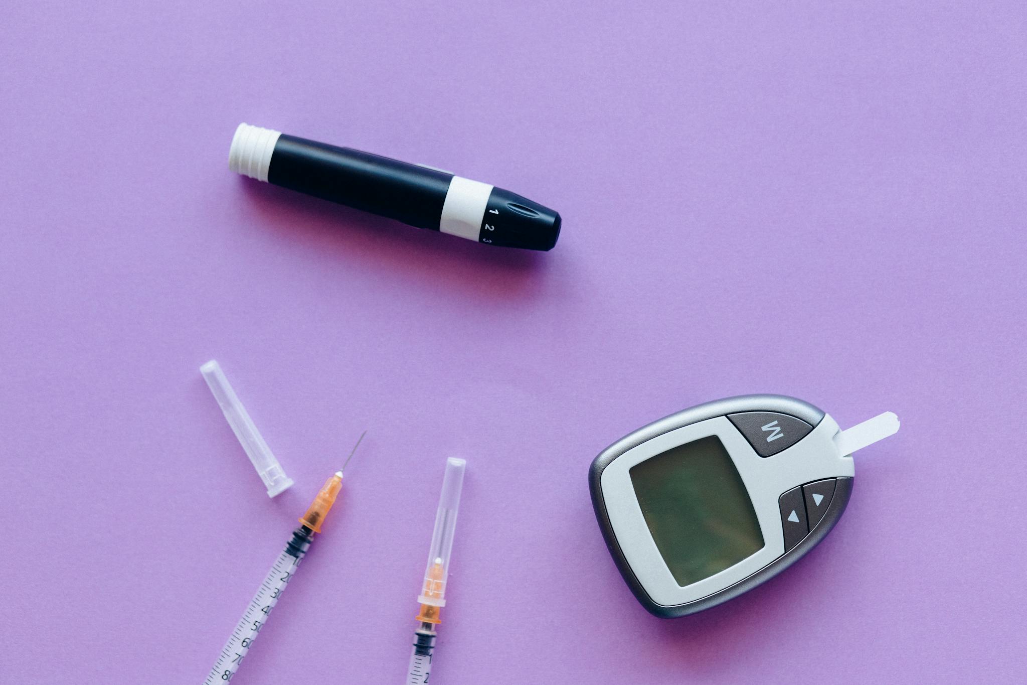 Top view of diabetes management tools including glucose meter and insulin syringes on purple background.